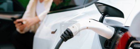 Photo for Young woman use smartphone to pay for electricity at public EV car charging station green city park. Modern environmental and sustainable urban lifestyle with EV vehicle. Panorama Expedient - Royalty Free Image