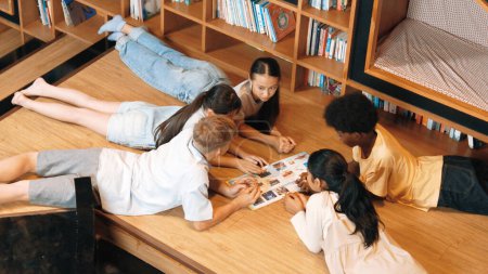 Photo for Group of diverse children lying down in circle while reading a book at library. Top view of girl sharing a magazine while pointing at interested topic and talking with lovely friends. Edification. - Royalty Free Image