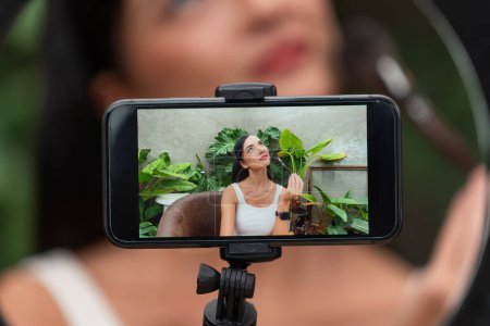 Photo for Rear view woman make natural beauty and cosmetic tutorial on green plant garden video content display on phone screen. Beauty blogger showing how to beauty care to social medial audience. Blithe - Royalty Free Image
