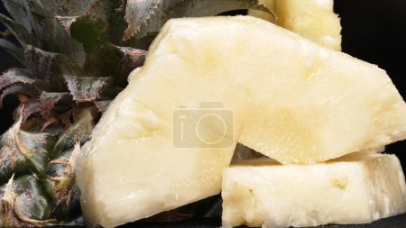 Close up video of fresh pineapple with slice of peel pineapple insert with separated black background. The rough and waxy rind, boasting a crown of spiky green leaves, Food photography. Comestible.