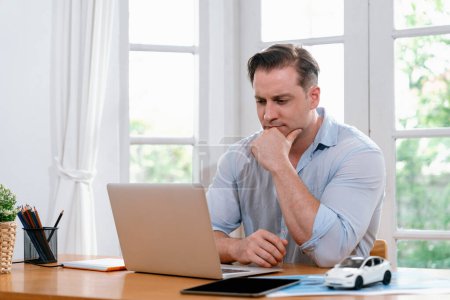Geschäftsmann müht sich, das Arbeitsproblem von zu Hause aus mit dem Laptop zu lösen, sitzt zu Hause mit gestresstem und frustriertem Gesichtsausdruck auf seinem Schreibtisch und versucht, eine Lösung für das Problem zu finden. Synchronos