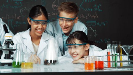 Mädchen beim Experimentieren an der Tafel mit Chemie-Theorie im MINT-Unterricht. Lehrer und eine Gruppe von High-School-Schülern mit gemischten Rassen machen gemeinsam naturwissenschaftliche Aktivitäten. Erbauung.