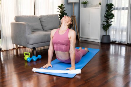 Flexible und geschickte Frau in Sportbekleidung, die Yogaposition in Meditationshaltung auf der Trainingsmatte zu Hause macht. Gesunde Fröhlichkeit zu Hause Yoga-Lebensstil mit friedlichem Geist und Gelassenheit.