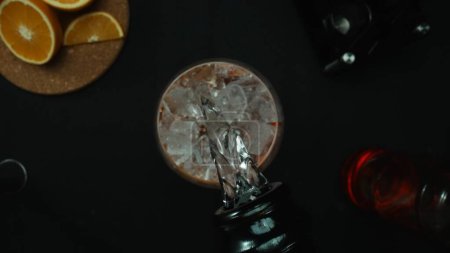 Macrografía, experimente el arte de mezclar un cóctel Negroni desde una perspectiva de arriba hacia abajo, adornado con una rebanada de naranja fresca y vibrante, todo sobre un fondo negro dramático. Alcohólico. Comestible.