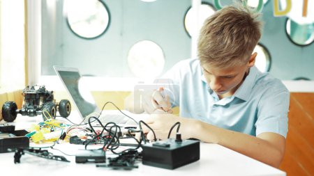 Photo for Caucasian boy fixing main board while study construction by using laptop analysis data. Young technician repairing and learning about using industrial structure at STEM technology class. Edification. - Royalty Free Image