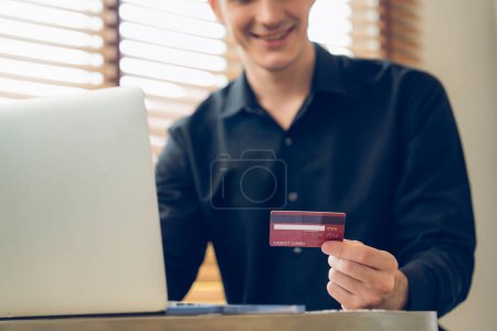 Photo for Young man using laptop with credit card for internet banking, online shopping E commerce by online payment gateway at home office. Modern and convenience online purchasing with debit card. Unveiling - Royalty Free Image