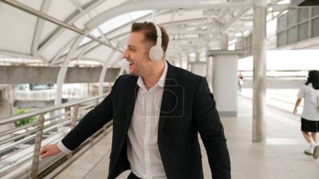 Photo for Happy business man dancing while wear headphone at bridge in urban city. Energetic manager cheerful and motivation performance moving to music to celebrate successful project while walk along. Urbane. - Royalty Free Image