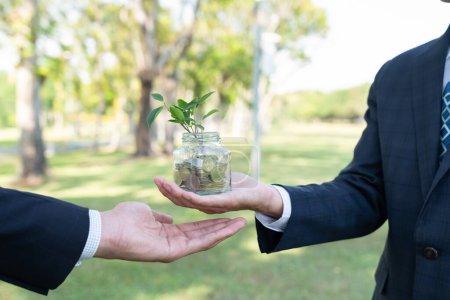 Konzept der nachhaltigen Geldanlage mit Glasgefäß gefüllt mit Sparmünzen bei Geschäftsleuten als umweltfreundliche Geldanlage, die mit der Natur und einem gesunden Ruhestand gepflegt wird. Kreisel