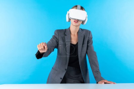 Téléchargez les photos : Chef de projet portant casque VR et debout tout en tenant l'hologramme de la technologie d'innovation. Femme d'affaires qualifiée se connecter avec le monde de la réalité visuelle tout en regardant les données pour l'investissement. Machines et appareils. - en image libre de droit