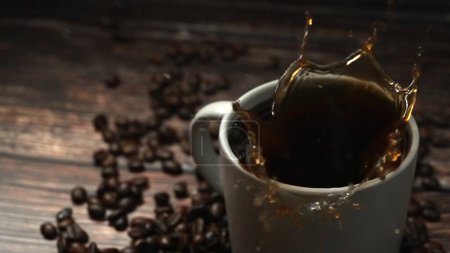 Téléchargez les photos : Chute d'espresso chaud dans une tasse à café décorée de piles de grains de café placées sur une table en bois entourée de fond noir. Gros plan du café chaud qui tombe au ralenti. Comestible. - en image libre de droit
