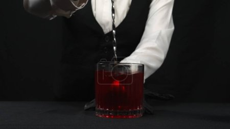 Macrography, observe the expertise of a bartender as stir a Rosemary Cranberry Martini against a striking black background. Each close-up shot captures of vibrant red cocktail. Alcoholics. Comestible.