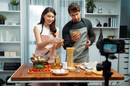Couple chef influencers on cooking show presenting ingredient of spaghetti, meat, chilli, tomato, garlic and seasoning sauces homemade special recipe recording on camera on live channel. Postulate.