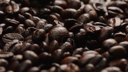 Macro shot of super slow motion shot of fresh coffee bean placed with black background. Close up of piles of aromatic roasted coffee seed surrounded. Macrography. Beans scattering around. Comestible.