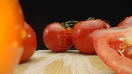Makrografie, Tomatenscheiben ruhen elegant auf einem rustikalen Schneidebrett vor dramatischem schwarzen Hintergrund. Jede Nahaufnahme fängt die saftige Konsistenz und die satten Farben der Tomaten ein. Komestibel.