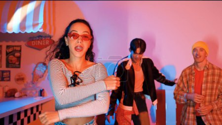 Atractiva bailarina caucásica mirando a la cámara mientras se mueve a la música hip hop. El equipo de baile diverso profesional realiza un movimiento enérgico y un paso loco en el estudio con luz led rosa. Regalamiento.