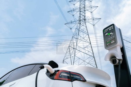 EV electric car at recharging at charging station connected to electrical power grid tower on sky background as electrical industry for eco friendly rechargeable vehicle utilization. Expedient