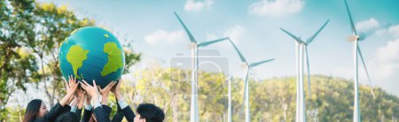 Téléchargez les photos : Concept de journée de la Terre avec un grand globe terrestre tenu par une équipe asiatique d'hommes d'affaires promouvant la sensibilisation à l'environnement en utilisant des énergies propres, durables et renouvelables avec des éoliennes pour un avenir plus vert. Pneumatique - en image libre de droit