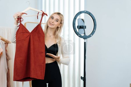 Photo for Young social medial content creator woman make fashion video. Blogger smiles to camera and light ring while making persuasive online clothing sell vlog to audience or follower. Blithe - Royalty Free Image