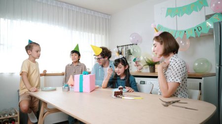 Photo for Caucasian mom cutting birthday cake and separated dessert while give to father. Happy family wear party hat to celebrated daughter birthday while sitting at table. Special occasion concept. Pedagogy. - Royalty Free Image