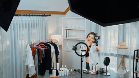 Photo for Woman influencer shoot live streaming vlog video review clothes prim social media or blog. Happy young girl with apparel studio lighting for marketing recording session broadcasting online. - Royalty Free Image