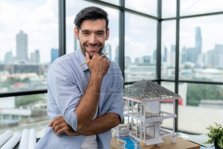 Photo for Portrait of happy skilled architect engineer in casual outfit smiling while looking at camera. Businessman posing at camera and standing near house model, architectural design, project plan. Tracery. - Royalty Free Image