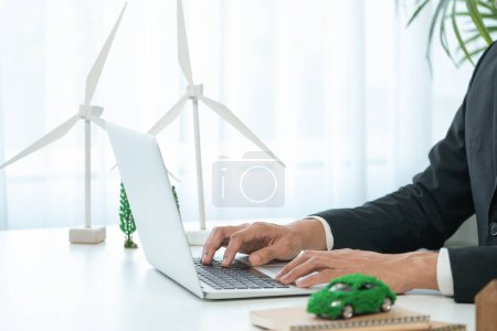 Un homme d'affaires travaillant dans un bureau élaborant un plan ou un projet d'entreprise sur une voiture écologique utilisant une technologie d'énergie alternative nette zéro sur ordinateur pour un environnement plus vert dans le cadre de l'effort de RSE. Pneumatique
