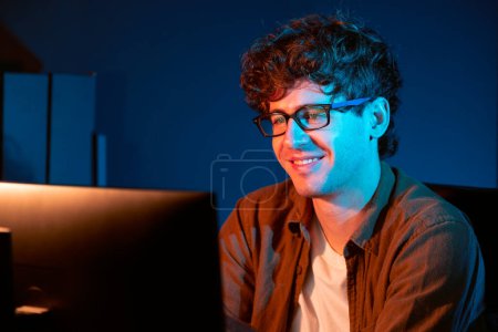 Photo for Smiling young businessman focusing on pc for creative startup project job at neon light modern office. Thinking marketing network online planning of creator to market channel design concept. Gusher. - Royalty Free Image