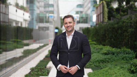 Photo for Happy caucasian business man smiling and looking at camera at urban city. Executive manager standing with confidence in green city while wear suit with blurred background. Green environment. Urbane. - Royalty Free Image