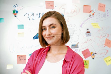 Portrait of young beautiful caucasian businesswoman smiling and posing with confident while looking at camera in front of whiteboard with mind map and colorful sticky notes. Closeup. Immaculate.