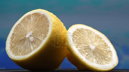 A slice of lemon, bright yellow and vibrantly citric, lies exposed. The yellow flesh, with refreshing juice, reveals its segmented interior. The essence of citrus vibrancy. Slow motion. Comestible.