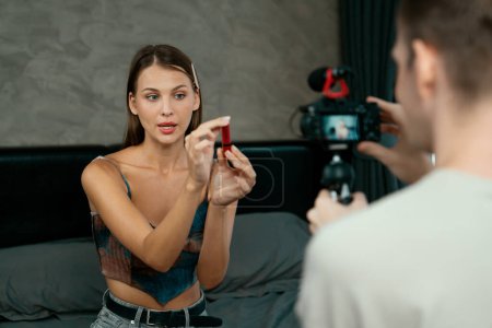 Téléchargez les photos : Homme filmant une vidéo sur une jeune femme faisant du contenu vidéo de tutoriel beauté et cosmétique pour les médias sociaux. Blogueur beauté sourit à la caméra tout en montrant comment les soins de beauté au public ou suiveur. Dévoilement - en image libre de droit