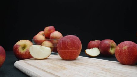 Téléchargez les photos : Macrographie de pommes présentées sous différentes formes : entières, tranchées, et dans un bol en verre avec fond noir. Chaque gros plan capture les couleurs rouges des pommes sur la planche à découper. Comestible. - en image libre de droit