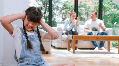 Photo for Stressed and unhappy young girl huddle in corner, cover her ears blocking sound of her parent arguing in background. Domestic violence at home and traumatic childhood develop to depression. Synchronos - Royalty Free Image