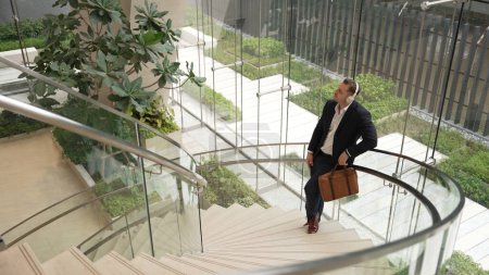 Photo for Top view of caucasian businessman listening relaxing music wearing headphone while standing at spiral stair cases at modern building. Project manager enjoy listening song while move to rhyme. Urbane. - Royalty Free Image
