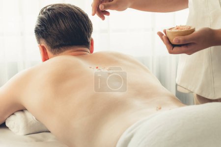 Téléchargez les photos : Homme heureux client ayant un traitement d'exfoliation dans un salon de spa de luxe avec lumière de bougie de chaleur ambiante. Sel gommage soin de beauté dans le gommage du corps spa de santé. Tranquillité - en image libre de droit