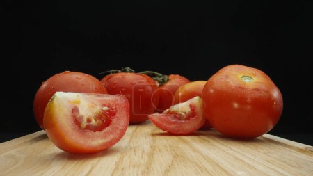 Téléchargez les photos : Macrographie, tranches de tomate reposent élégamment sur une planche à découper rustique sur un fond noir dramatique. Chaque gros plan capture la texture juteuse et les couleurs riches des tomates. Comestible. - en image libre de droit