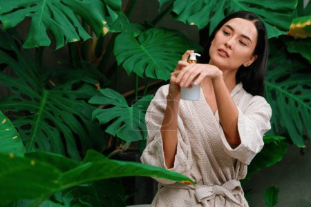 Tropical and exotic spa garden with bathtub in modern hotel or resort with woman in bathrobe holding beauty skincare product while enjoying leisure lush with greenery foliage background. Blithe