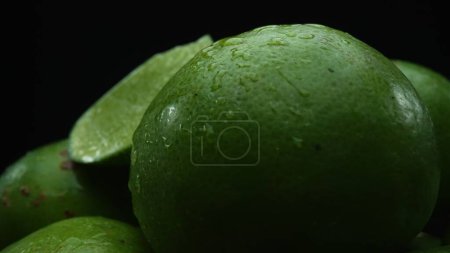 Slices of lime are meticulously arranged in a pile, set against a black background. Each lime slice is captured in stunning detail, its vibrant green hue and enticing texture. Close up. Comestible.