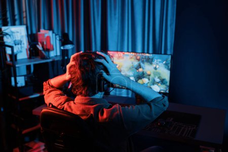 Host-Kanal von stressigen jungen Gaming-Streamer immer im Kampf gegen Moba in der Schlacht Arena besiegt Multiplay-Team zu verlieren, trägt Kopfhörer auf dem PC-Monitor mit Rückseite Bild in roten Neon-Raum. Gusher.