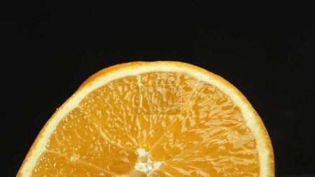 Foto de Una captura macrográfica de una rebanada de naranja, colocada sobre un fondo negro elegante y aislado, se despliega como una obra maestra visual de encanto cítrico. Una rebanada de naranja con fondo negro. Comestible. - Imagen libre de derechos