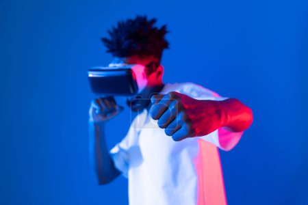 Afroamerikanische Box-Spieler tragen VR spielende Boxerspiel Kasperlkamera posiert isoliert blau rosa Neonlicht Wand verbindet futuristische Technologie Virtual Reality metaverse Fighting Box. Beitrag.