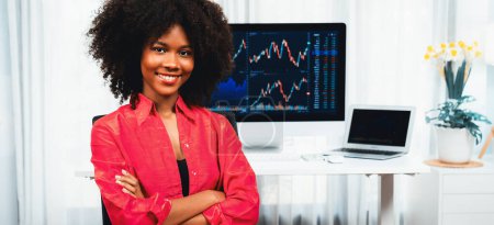 Téléchargez les photos : Analytique jeune femme d'affaires afro-américaine, spécialiste du trading boursier réussi, contre graphique de données dynamiques affichant l'analyse des tendances marketing à l'écran. Tastemaker. - en image libre de droit