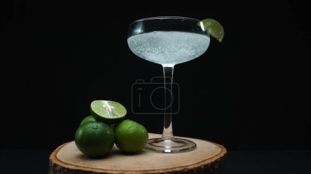 Macrography, eine verlockende Margarita, wird in einem Glas eingefangen, das mit einer lebendigen Limettenscheibe garniert ist, alles vor einem fesselnden schwarzen Hintergrund. Jede Nahaufnahme von Cocktail und Limette. Komestibel.