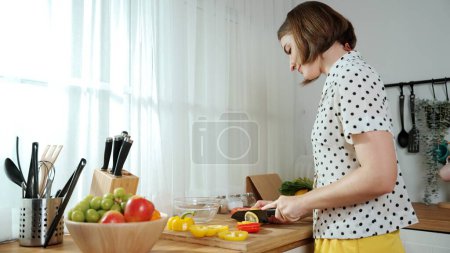 Téléchargez les photos : Mère énergique faisant la salade pour le petit déjeuner à la cuisine moderne tout en hachant des légumes entourés d'ustensiles de cuisine. Femme intelligente gardien de maison cuisine et la préparation des aliments. Mode de vie sain. Pédagogie. - en image libre de droit