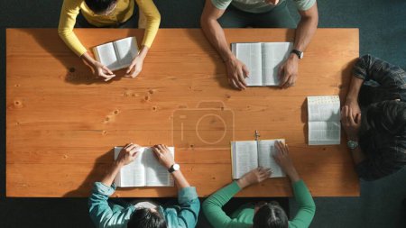 Photo for Top view of prayer reading books while prays to god at table with bible and cross placed with faith, spirituality and religion. Aerial view of diverse people holding and looking at bible. Symposium. - Royalty Free Image