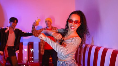 Amigo multicultural bailando juntos y moviéndose a lo largo de la música hiphop mientras están de pie en el restaurante o cafetería con luz de neón rosa. El grupo profesional de bailarinas callejeras realiza un movimiento enérgico. Regalamiento.