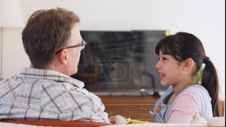 Grandfather and granddaughter together watch interesting entertainment media on TV. Old senior use technology communicate with young generation cross generation gap strengthen family bond. Divergence.