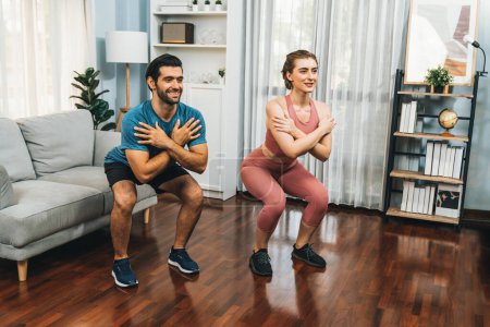 Athletic and sporty couple doing squat together during home body workout exercise session for fit physique and healthy sport lifestyle at home. Gaiety home exercise workout training concept.