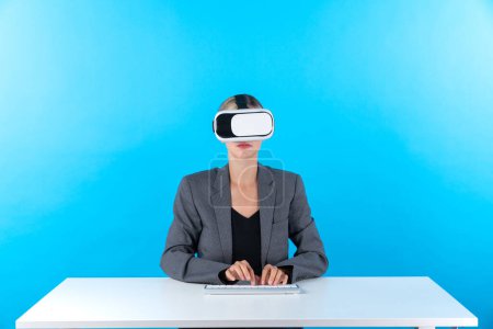 Téléchargez les photos : Smart manager portant des lunettes VR assis à table avec clavier. Femme d'affaires pointant pour gérer l'analyse de données tout en utilisant costume et casque de réalité visuelle et entrer en métaverse. Machines et appareils. - en image libre de droit