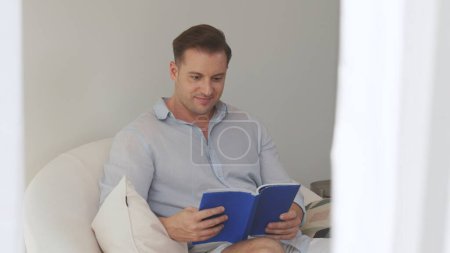 Mann mittleren Alters, der auf dem Sofa sitzt und Lehrbücher liest, vertieft sein Wissen über soziale und technologische Berufe oder erzieht Kinder, um als kluger Vater ein guter Erwachsener zu sein. Konzept des lebenslangen Lernens. Divergenz.